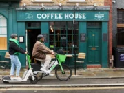Two Lime riders using an electric scooter and e-bike outside a coffee shop