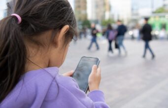 Ofcom Pushes Meta, Snap And Roblox On Child Safety Little girl using a smartphone in public for Ofcom child safety story
