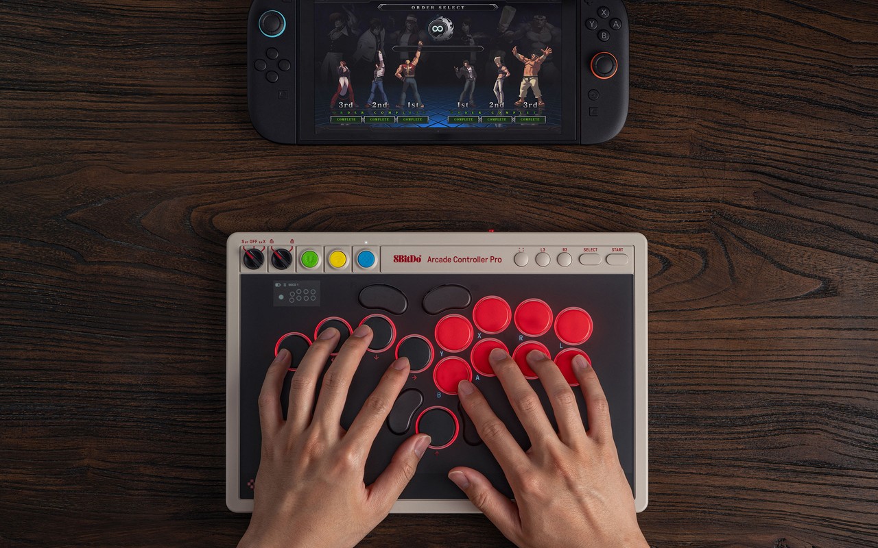 Hands on the 8BitDo Arcade Controller Pro leverless all-button layout, a fighting game on the handheld behind it