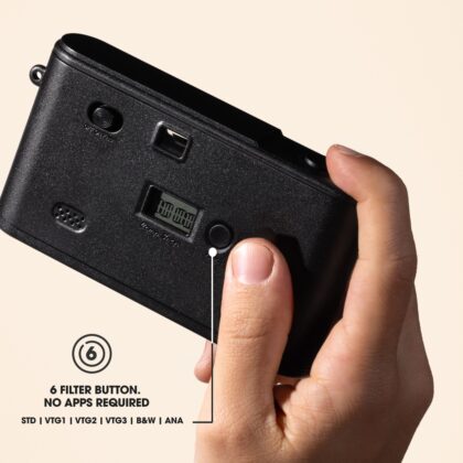 A hand holding the back of the Camp Snap 2 camera with the filter button and paper display visible.