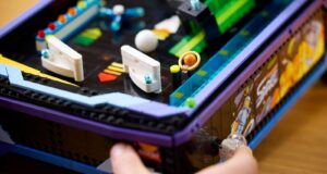 A hand plays the LEGO Icons Arcade Pinball Machine, LEGO set 11374, showing its working launcher and tabletop arcade design.