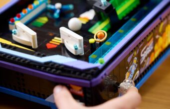 A hand plays the LEGO Icons Arcade Pinball Machine, LEGO set 11374, showing its working launcher and tabletop arcade design.