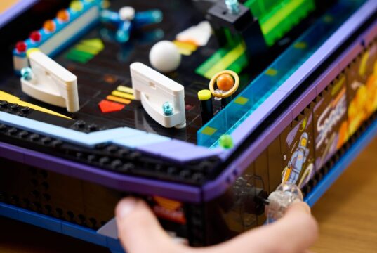 A hand plays the LEGO Icons Arcade Pinball Machine, LEGO set 11374, showing its working launcher and tabletop arcade design.