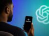 OpenAI Reportedly Files Confidential SEC Paperwork to Go Public African American man holding a phone showing OpenAI branding for IPO news