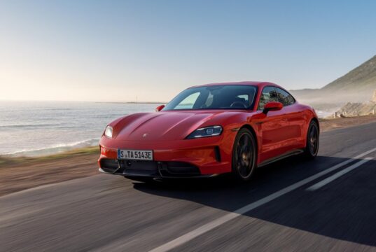 Red Porsche Taycan driving on a coastal road.