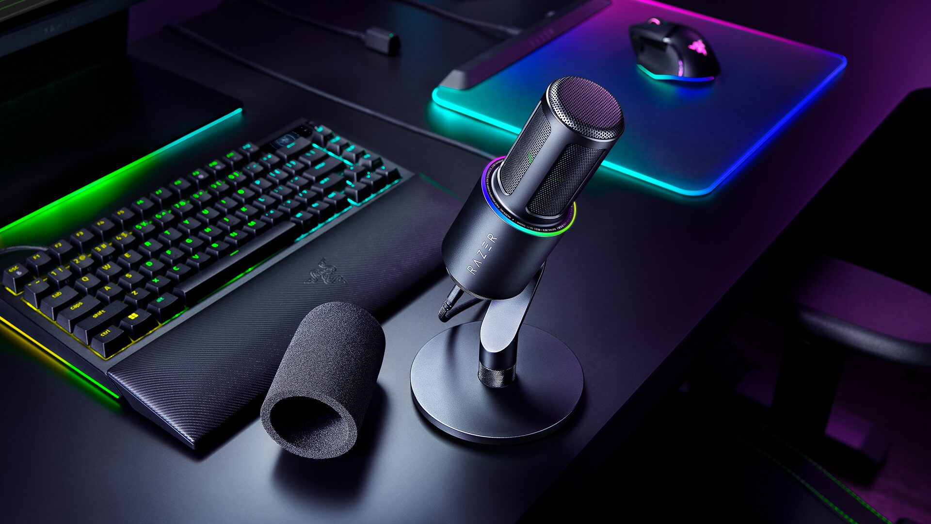 Razer Seiren V3 Pro microphone with its removable foam pop filter beside a RGB gaming setup
