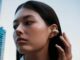 Sennheiser ACCENTUM Clip Takes Open-Ear Earbuds Into LDAC Territory Person wearing cream Sennheiser ACCENTUM Clip open-ear earbuds on a city street.
