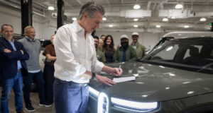 California EV rebate announcement with Gov. Gavin Newsom signing legislation beside a Rivian vehicle