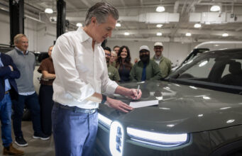California EV Rebate: MyFirstEV Offers $3,500 to New Buyers California EV rebate announcement with Gov. Gavin Newsom signing legislation beside a Rivian vehicle