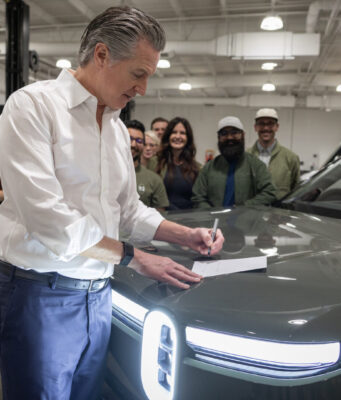 California EV Rebate: MyFirstEV Offers $3,500 to New Buyers California EV rebate announcement with Gov. Gavin Newsom signing legislation beside a Rivian vehicle