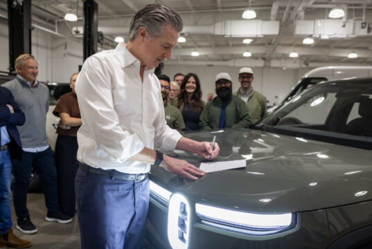 California EV rebate announcement with Gov. Gavin Newsom signing legislation beside a Rivian vehicle