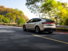 Tesla Model Y Long Wheelbase Brings Six Seats to the US for $61,990 Tesla Model Y Long Wheelbase driving on a tree-lined road, rear three-quarter view