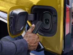 Every 2027 GM EV Will Plug Into Tesla Superchargers Official GM photo of a NACS charger plug at the charge port of a yellow GMC Hummer EV