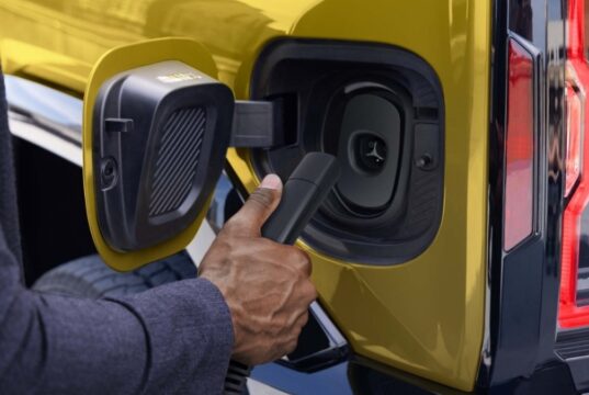 Official GM photo of a NACS charger plug at the charge port of a yellow GMC Hummer EV
