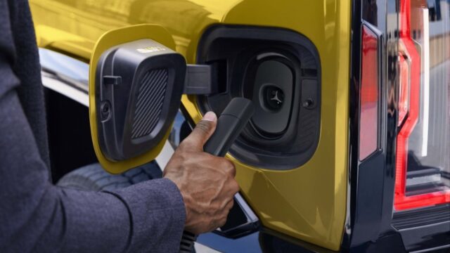 gm-2027-nacs-hummer-port Official GM photo of a NACS charger plug at the charge port of a yellow GMC Hummer EV