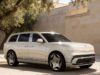 Cream Genesis GV90 three-quarter front view beside a stone wall and olive tree