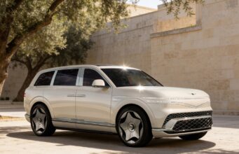 Genesis GV90 Neolun Flagship EV SUV Debuts With Coach Doors Cream Genesis GV90 three-quarter front view beside a stone wall and olive tree