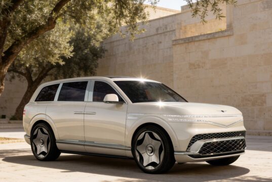Cream Genesis GV90 three-quarter front view beside a stone wall and olive tree