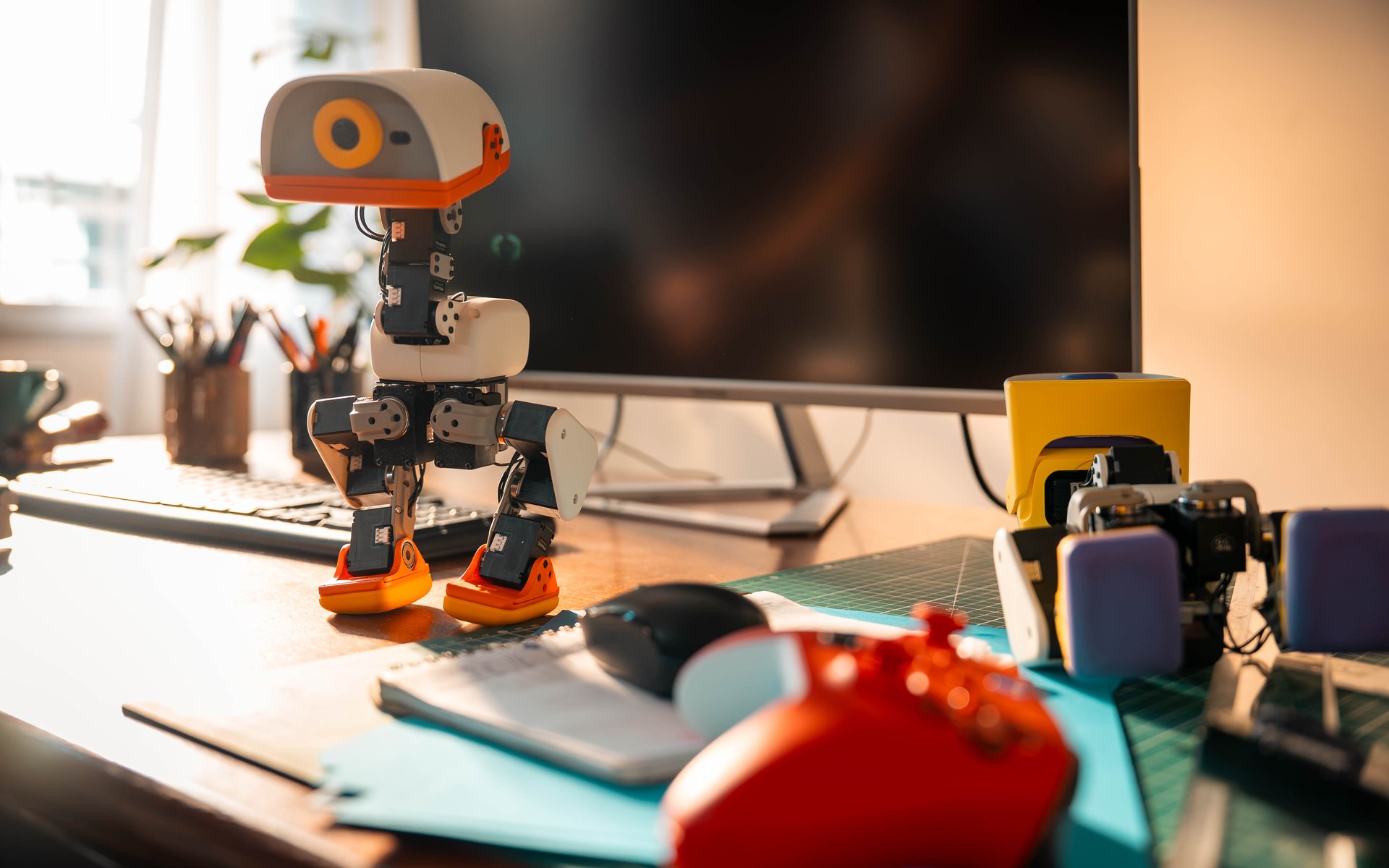 Cream Microduck standing on a sunlit desk next to a monitor and a game controller