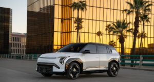 White 2027 Kia EV3 parked in front of a gold-glass office building at sunset