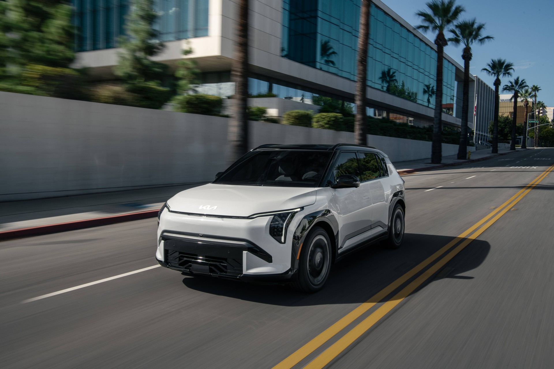 White 2027 Kia EV3 driving on a city street lined with palm trees