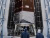 Technicians in blue clean-room suits stand before NASA's Nancy Grace Roman Space Telescope inside open Falcon Heavy fairing halves