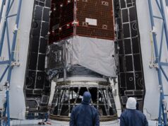 Technicians in blue clean-room suits stand before NASA's Nancy Grace Roman Space Telescope inside open Falcon Heavy fairing halves