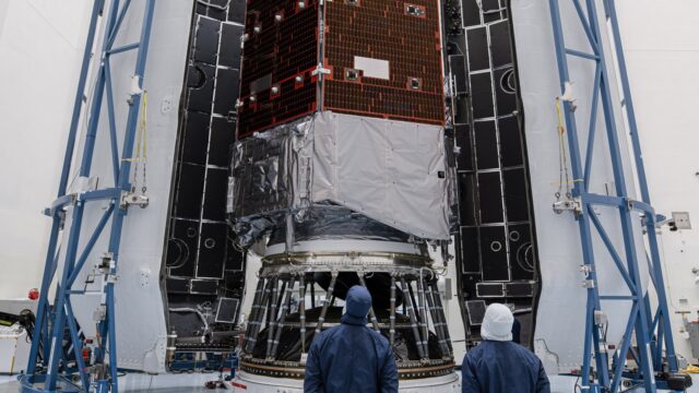 roman-fairing-featured Technicians in blue clean-room suits stand before NASA's Nancy Grace Roman Space Telescope inside open Falcon Heavy fairing halves