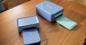 Cricut StickerPix Print and Print + Cut machines on a wooden table with output trays open