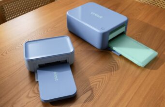 Cricut StickerPix Print and Print + Cut machines on a wooden table with output trays open