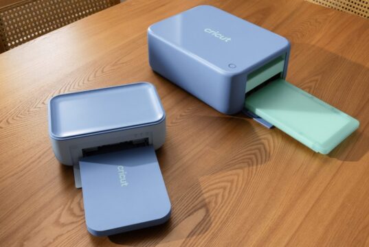 Cricut StickerPix Print and Print + Cut machines on a wooden table with output trays open