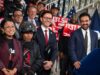 Mayor Zohran Mamdani and officials standing with delivery workers holding red $131.5 million signs at City Hall