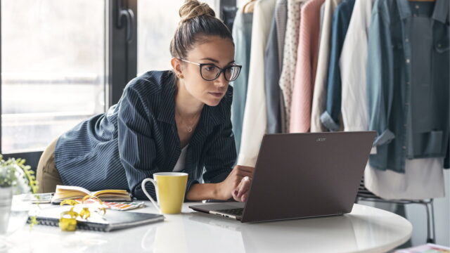 featured-2 Acer Vero 16 laptop open on a white table while its owner works in a bright studio.