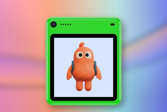 Freckle phone in green with an orange character on its screen against a coral and blue editorial background