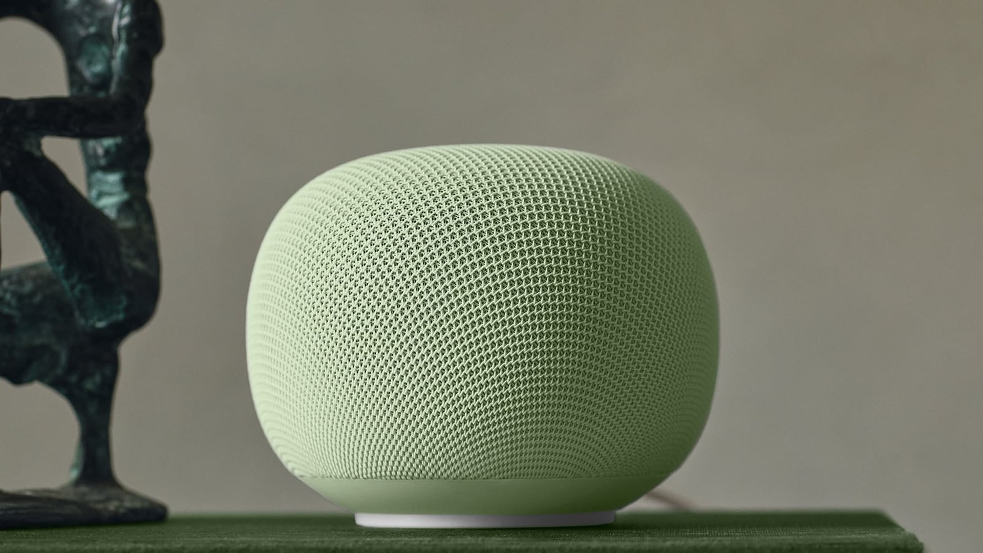 Sage green Google Home Speaker sitting on stacked books beside a bronze sculpture