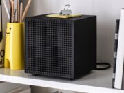 IKEA Badkruka Speaker: $59.99 Wired Bluetooth Audio Black IKEA Badkruka cube speaker on a white shelf between books and a yellow pencil holder, with its power cable behind it