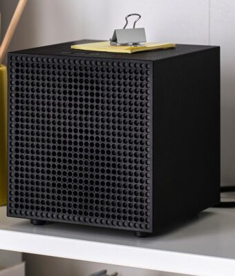 IKEA Badkruka Speaker: $59.99 Wired Bluetooth Audio Black IKEA Badkruka cube speaker on a white shelf between books and a yellow pencil holder, with its power cable behind it
