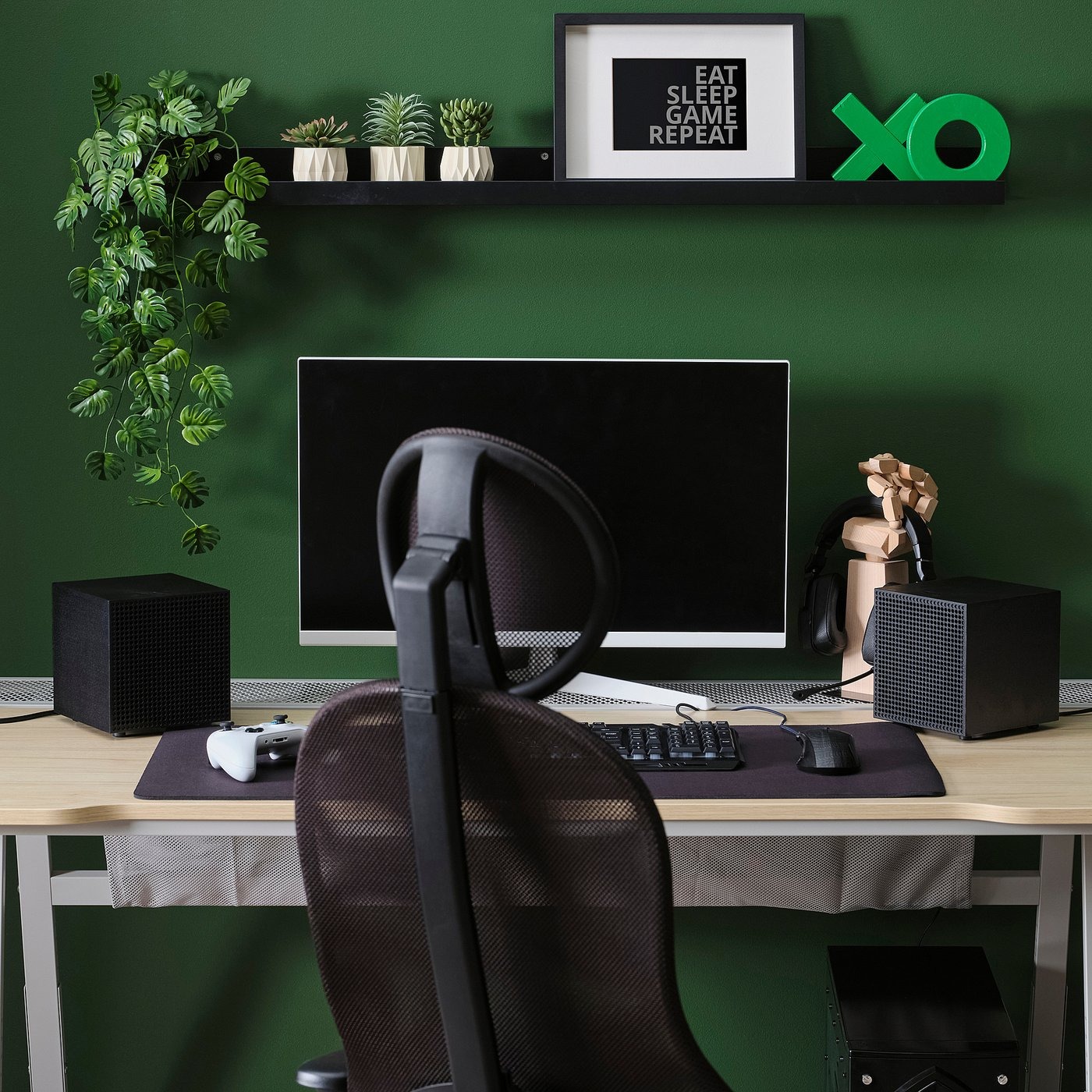 Two black IKEA Badkruka speakers on either side of a monitor on a gaming desk against a green wall
