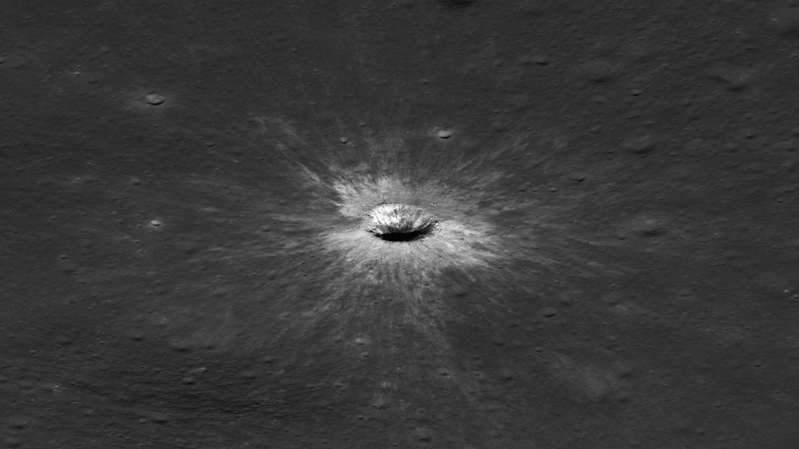 Oblique black-and-white view of McGetchin crater as a small bright bowl with pale rays spreading across dark lunar terrain