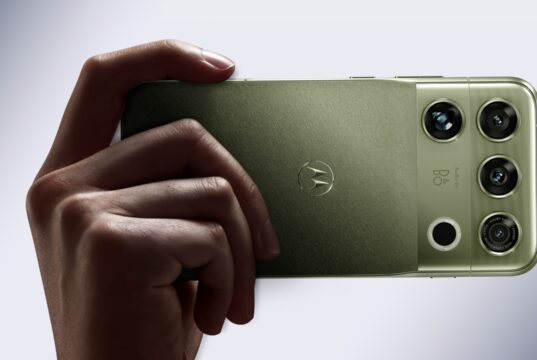 Motorola Signature 27 in PANTONE Capulet Olive held in hand, showing its quad camera housing with B&O branding