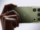 Motorola Signature 27 in PANTONE Capulet Olive held in hand, showing its quad camera housing with B&O branding