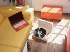 Packard Bell Is Back Under Acer With a €499 DotBook, but Only in Europe Orange Packard Bell DotBook laptop on a yellow sofa beside the DotLoop suitcase turntable