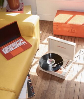 Packard Bell Is Back Under Acer With a €499 DotBook, but Only in Europe Orange Packard Bell DotBook laptop on a yellow sofa beside the DotLoop suitcase turntable