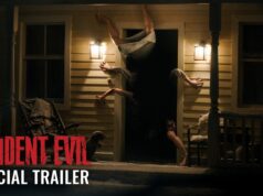 A figure contorted upside down in the doorway of a lit farmhouse porch at night, from Sony's Resident Evil official trailer