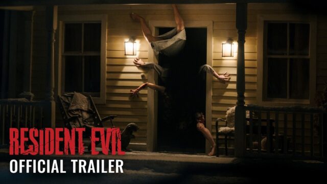 A figure contorted upside down in the doorway of a lit farmhouse porch at night, from Sony's Resident Evil official trailer