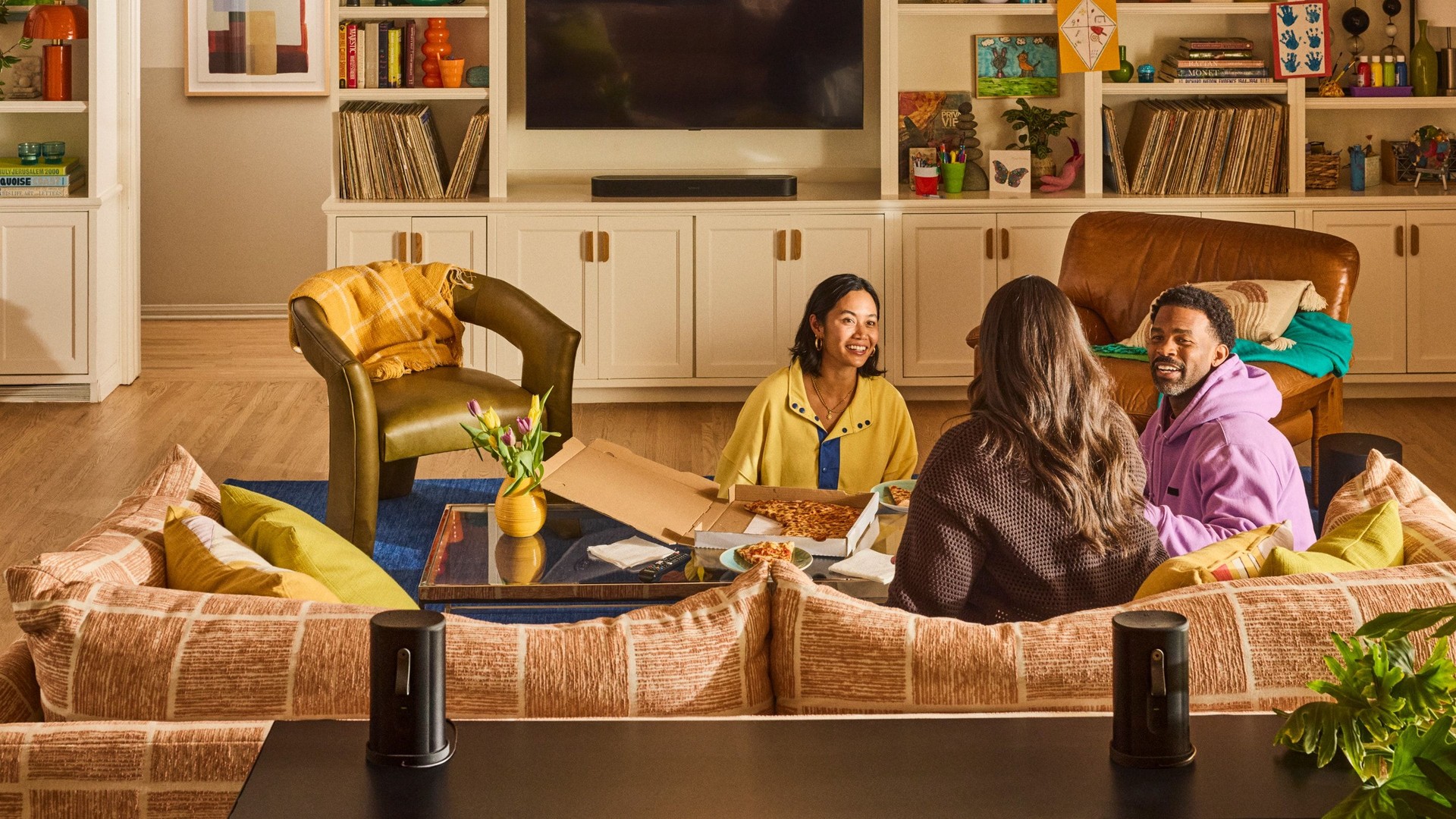 Two black portable Sonos speakers on a sofa back in a living room with a soundbar under the TV