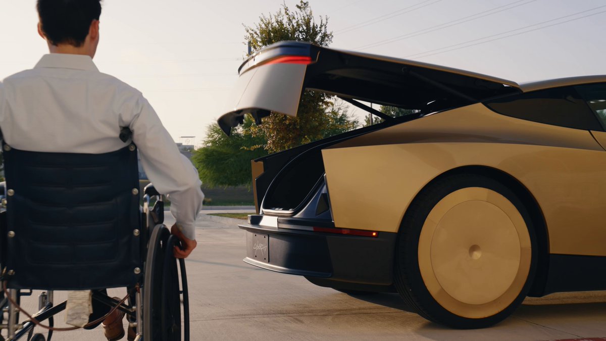 Official Tesla still of a gold Cybercab with its trunk open beside a rider using a wheelchair