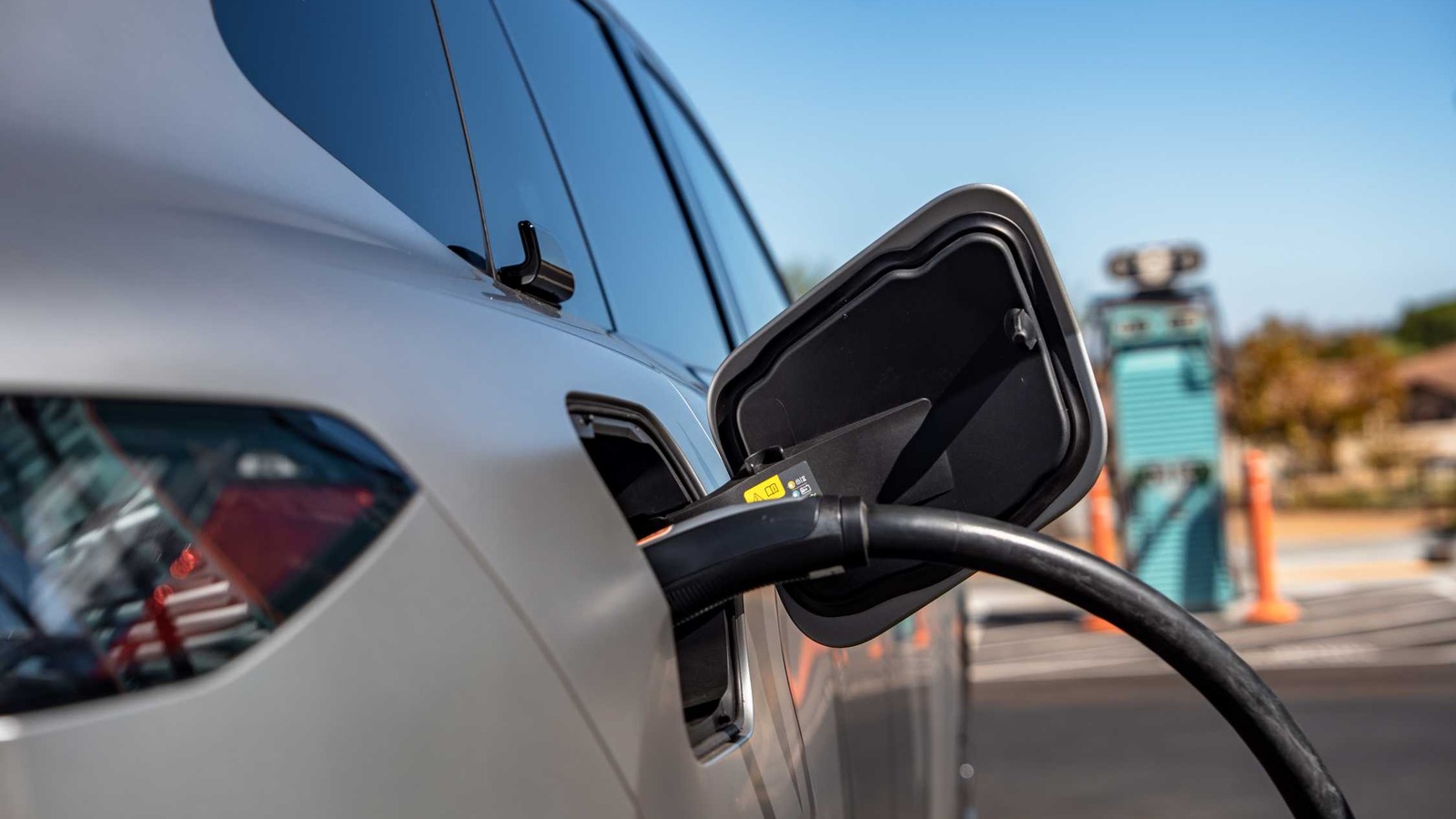 Close-up of the 2027 BMW iX5 60 xDrive high-power charging cable plugged into the rear charge port below the B-pillar Winglet door handle
