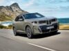 2027 BMW iX5 60 xDrive Starts at $79,800 With an Estimated 435-Mile Range and 460 kW Charging 2027 BMW iX5 60 xDrive driving along a coastal mountain road showing its illuminated vertical kidney grille and B-pillar Winglet door handles