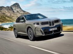 2027 BMW iX5 60 xDrive driving along a coastal mountain road showing its illuminated vertical kidney grille and B-pillar Winglet door handles